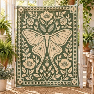 May include: A rectangular woven tapestry featuring a large central moth with long, trailing wings. The design is rendered in cream-colored thread against a deep forest green background, surrounded by a floral border of roses and poppy buds.