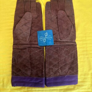 May include: A pair of brown suede gloves with a quilted pattern on the lower portion and a purple cuff. The gloves have a tag that reads "Costume Replicas".