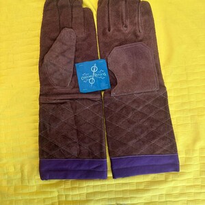 May include: A pair of brown suede gloves with quilted diamond stitching on the lower arm. The gloves have a purple band at the wrist and a blue tag that reads "Costume Replicas".