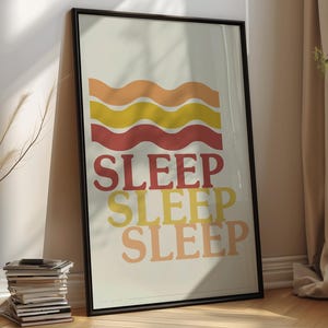 Peut inclure: Impression d'art encadrée avec le mot "SLEEP" dans une police rétro. L'œuvre présente des lignes ondulées orange, jaune et rouge au-dessus du mot. L'impression est dans un cadre noir et est appuyée contre un mur.