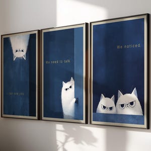 May include: A set of three framed wall art prints featuring white cats against a deep blue background. The first print shows a cat hanging upside down with the text I can see you. The second shows a cat peeking with We need to talk. The third shows two cats with We noticed.