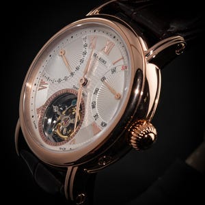 May include: A rose gold wristwatch with a white face and black leather band. The watch face features Roman numerals, day and date indicators, and a visible tourbillon mechanism. The watch is marked "SEA-KORS" and "MADE IN CHINA".