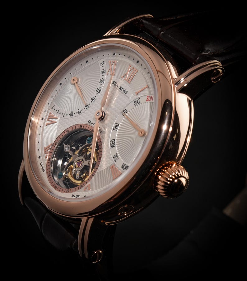 May include: A rose gold wristwatch with a white face and black leather band. The watch face features Roman numerals, day and date indicators, and a visible tourbillon mechanism. The watch is marked "SEA-KORS" and "MADE IN CHINA".