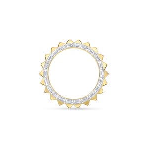 May include: A gold ring with a sunburst design. The ring features a band of rectangular, clear stones set within a circle. The outer edge has triangular gold prongs, creating a sun-like appearance. The ring is set against a white background.