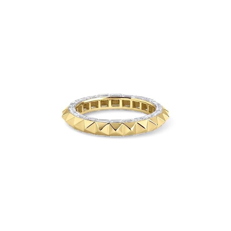 May include: A gold ring with a band of white gemstones and a row of gold pyramid-shaped studs. The ring is set against a white background.