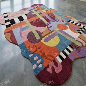 May include: A large, abstract area rug with a unique, freeform shape. The rug features a vibrant mix of colors including blue, orange, purple, and green, with geometric and organic shapes. The rug's design includes checkerboard patterns and curved lines.