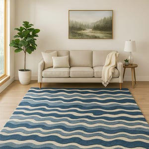 Pu&ograve; includere: Un tappeto blu e bianco a motivi con un design a onde in un soggiorno. Il tappeto presenta fasce di blu chiaro e scuro, creando un effetto fluido. Un divano beige, una pianta in vaso e un dipinto di paesaggio completano la scena. Dimensioni del tappeto: circa 240 cm x 300 cm.