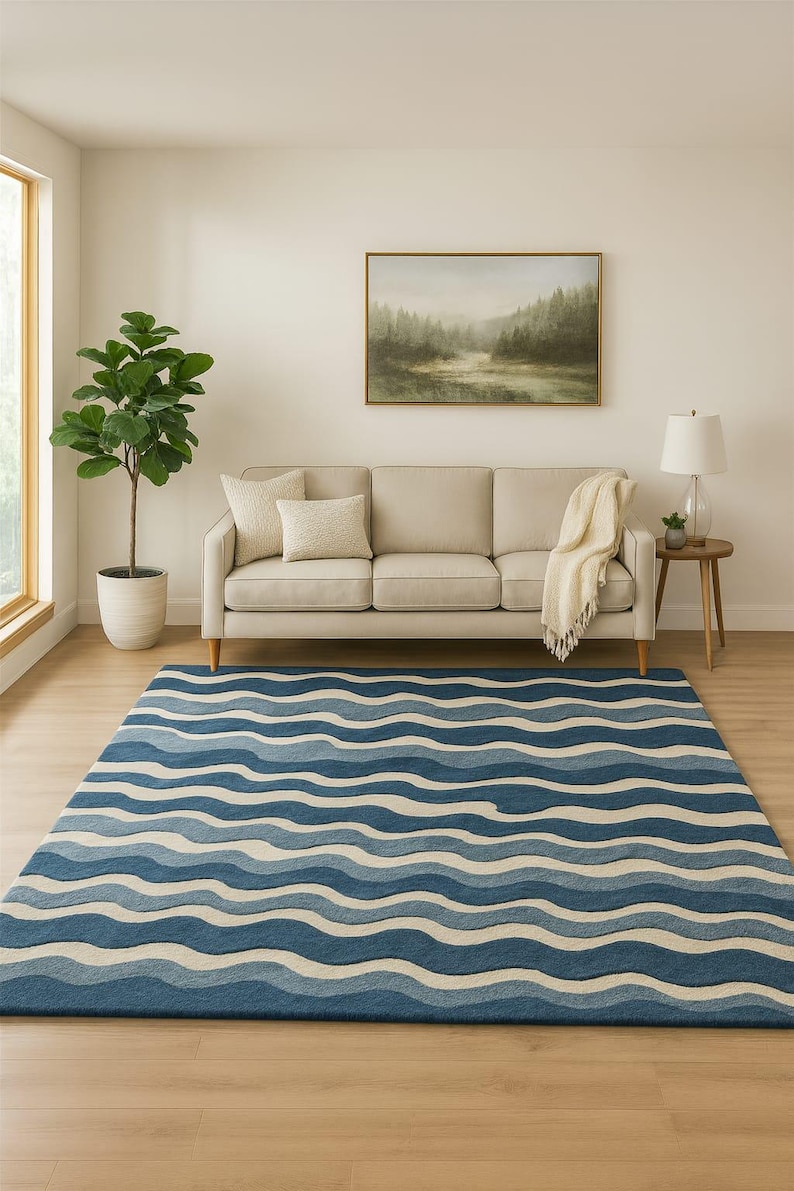 Pu&ograve; includere: Un tappeto blu e bianco a motivi con un design a onde in un soggiorno. Il tappeto presenta fasce di blu chiaro e scuro, creando un effetto fluido. Un divano beige, una pianta in vaso e un dipinto di paesaggio completano la scena. Dimensioni del tappeto: circa 240 cm x 300 cm.