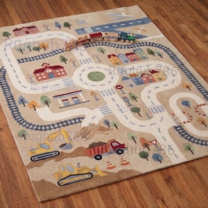 May include: A rectangular area rug with a beige background featuring a colorful town scene. The design includes white roads, dark blue train tracks, a circular roundabout, various buildings, trees, construction vehicles, and an airplane.