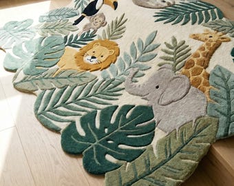 May include: An irregularly shaped area rug featuring a jungle theme with a cream background. The rug displays tufted illustrations of a toucan, a monkey, a lion, a sloth, an elephant, and a giraffe surrounded by various green tropical leaves.