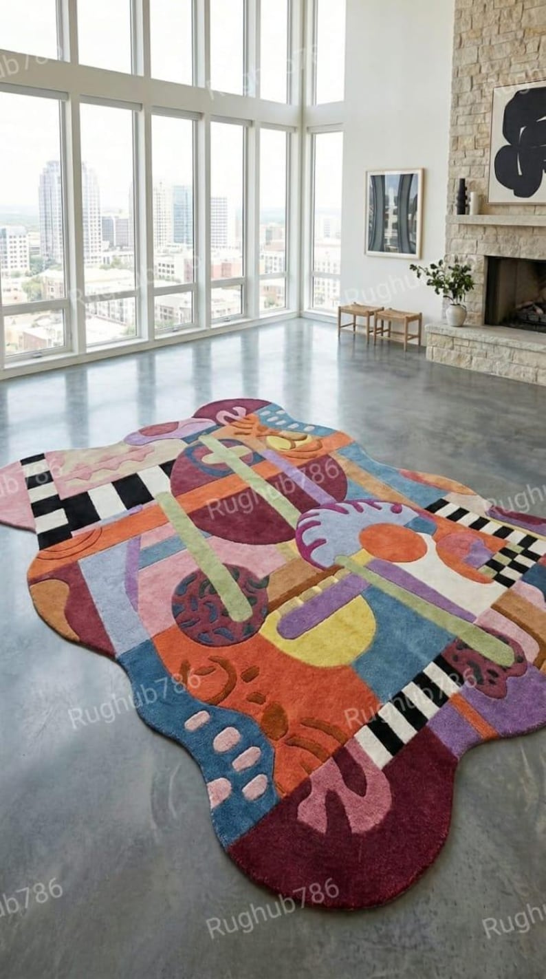 May include: A large, abstract area rug with a unique, freeform shape. The rug features a vibrant mix of colors including blue, orange, purple, and green, with geometric and organic shapes. The rug's design includes checkerboard patterns and curved lines.