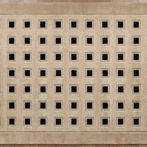 May include: A rectangular area rug featuring a beige textured surface with a repeating grid pattern of small, solid black squares arranged in eight rows and ten columns, framed by a wide, solid beige border along all four edges.