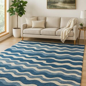 Pu&ograve; includere: Un tappeto blu e bianco a fantasia con un motivo a onde. Il tappeto si trova in un soggiorno con un divano beige, cuscini e un dipinto sulla parete. &Egrave; visibile una pianta in vaso.