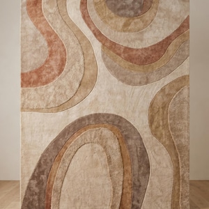 May include: A rectangular area rug with a beige background and a pattern of layered, curved shapes in shades of brown and tan. The rug's design features a soft, textured surface, adding visual interest and warmth to any room.