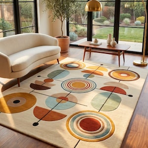 Può includere: Un tappeto rettangolare con sfondo color crema caratterizzato da un motivo geometrico di cerchi concentrici, semicerchi e sottili linee nere in tonalità giallo senape, arancione terracotta, verde salvia e azzurro su tutto il design.