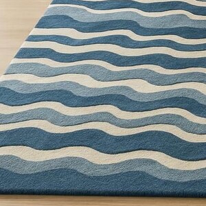 Pu&ograve; includere: Tappeto blu e bianco con motivo a onde. Il tappeto presenta fasce alternate di diverse tonalit&agrave; di blu e bianco, creando un design strutturato che evoca l'oceano. Il tappeto &egrave; realizzato in materiale morbido ed &egrave; adatto per uso interno.