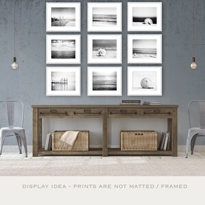 Puede incluir: Nueve impresiones en blanco y negro enmarcadas de escenas de playa exhibidas sobre una consola de madera. Las impresiones presentan vistas al oc&eacute;ano, conchas marinas y un muelle. Dos sillas de metal y cestas de mimbre completan la decoraci&oacute;n costera.