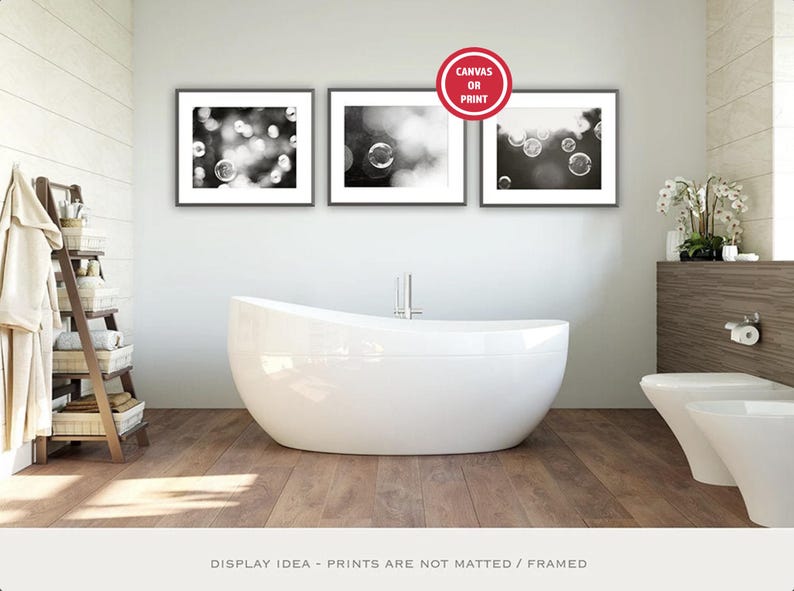 May include: A contemporary bathroom with three framed monochrome bubble art prints above a white, oval bathtub. A wooden ladder with towels and a toilet are also visible. The image suggests a spa-like atmosphere.