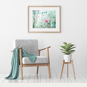 Pode incluir: Uma impress&atilde;o floral emoldurada com flores rosa e azuis. A impress&atilde;o &eacute; exibida acima de uma poltrona cinza com uma manta verde-azulado. Uma planta em vaso est&aacute; em um suporte de madeira. O quarto tem paredes e piso brancos.