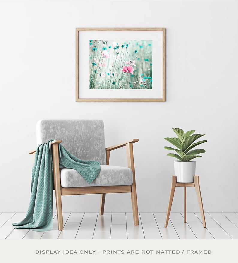 Pode incluir: Uma impress&atilde;o floral emoldurada com flores rosa e azuis. A impress&atilde;o &eacute; exibida acima de uma poltrona cinza com uma manta verde-azulado. Uma planta em vaso est&aacute; em um suporte de madeira. O quarto tem paredes e piso brancos.