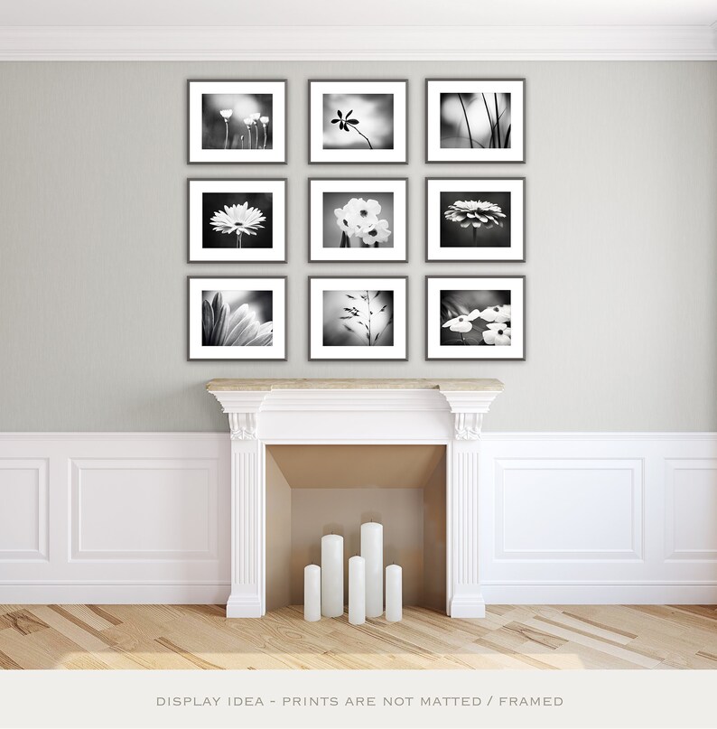 May include: A display idea for nine black and white framed photographs of flowers. The photos are arranged in a grid pattern on a light gray wall above a white fireplace with four white candles.