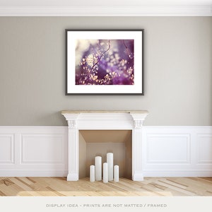 Pu&ograve; includere: Una stampa artistica incorniciata con un primo piano di una pianta con piccole foglie chiare e fiori viola e bianchi. L'opera d'arte &egrave; esposta sopra un camino bianco con cinque candele bianche. La stanza ha pareti di colore chiaro e un pavimento in legno.