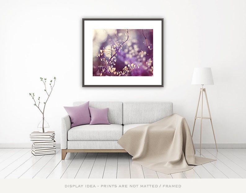 Pu&ograve; includere: Una stampa artistica incorniciata con un primo piano di fogliame viola. L'opera d'arte &egrave; sopra un divano grigio chiaro con due cuscini lavanda e una coperta beige. Una moderna lampada da terra e una pianta decorativa completano la stanza.
