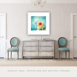 May include: A framed floral print featuring a vibrant orange and yellow dahlia against a teal and turquoise background. The artwork is displayed above a distressed gray chest of drawers, flanked by two teal upholstered chairs. The text at the bottom reads: DISPLAY IDEA - PRINTS ARE NOT MATTED / FRAMED.