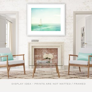 May include: A framed print of a sailboat on the ocean hangs above a fireplace. Two armchairs with light blue pillows sit on a patterned rug. A glass coffee table and white brick wall complete the scene.