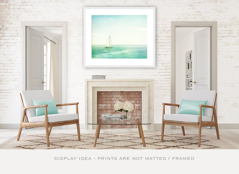 May include: A framed print of a sailboat on the ocean hangs above a fireplace. Two armchairs with light blue pillows sit on a patterned rug. A glass coffee table and white brick wall complete the scene.