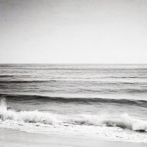 Puede incluir: Fotograf&iacute;a en blanco y negro del oc&eacute;ano. La imagen captura el mar con suaves olas que rompen en la orilla. El cielo es de un gris p&aacute;lido y el agua de un tono m&aacute;s oscuro, creando una escena costera serena y minimalista.