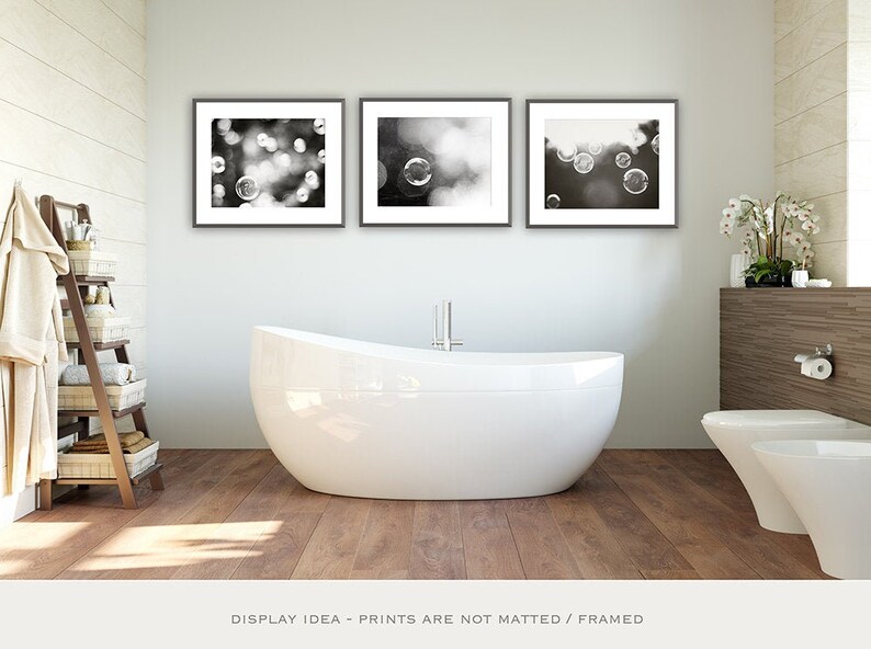 Three black and white framed photographs of blurry bubbles in a bathroom setting. The photographs are hung above a white bathtub and a white toilet. Available as a fine art print or canvas.