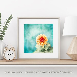 May include: A framed print featuring a close-up of an orange and red dahlia flower against a teal background. The print is displayed on a shelf with a white vase, eucalyptus, a gold alarm clock, and a geometric lamp. The text "DISPLAY IDEA - PRINTS ARE NOT MATTED / FRAMED" is at the bottom.