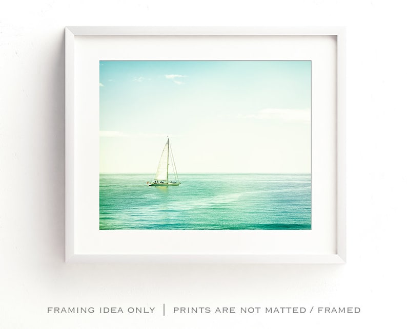 May include: A framed print of a sailboat on the ocean. The image features a white sailboat with its sails up, sailing on turquoise water under a light blue sky. The frame is white, and the text at the bottom reads "FRAMING IDEA ONLY | PRINTS ARE NOT MATTED / FRAMED."
