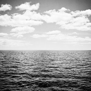 Puede incluir: Fotograf&iacute;a en blanco y negro del oc&eacute;ano bajo un cielo nublado. El agua oscura est&aacute; ondulada, con una l&iacute;nea de horizonte clara. El cielo est&aacute; lleno de nubes blancas y esponjosas, creando una escena natural.