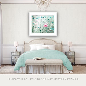 Pode incluir: Uma cena de quarto com uma impress&atilde;o floral emoldurada sobre uma cama com um edredom azul claro. A impress&atilde;o mostra flores rosa e azuis. Duas mesinhas de cabeceira espelhadas com l&acirc;mpadas ladeiam a cama. Um banco e um livro aberto est&atilde;o aos p&eacute;s da cama. O texto "DISPLAY IDEA - PRINTS ARE NOT MATTED / FRAMED" est&aacute; na parte inferior.