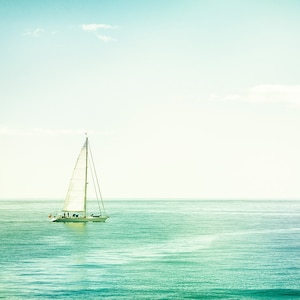 May include: A white sailboat with a tall mast and billowing sails glides across the turquoise ocean under a clear, light blue sky. The image evokes a sense of tranquility and adventure, with the boat as the central focus.