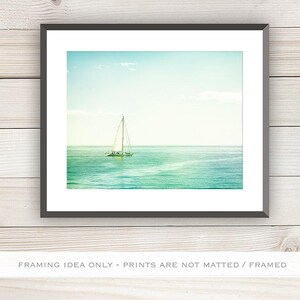 May include: A framed print featuring a sailboat on the ocean under a blue sky. The water transitions from turquoise to deep blue. The image is framed in a black border and set against a white background.