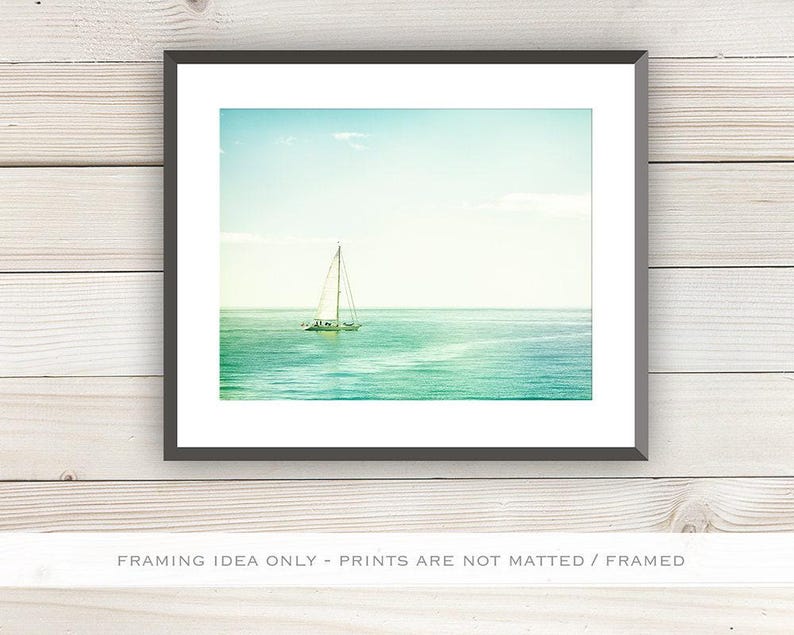 May include: A framed print featuring a sailboat on the ocean under a blue sky. The water transitions from turquoise to deep blue. The image is framed in a black border and set against a white background.