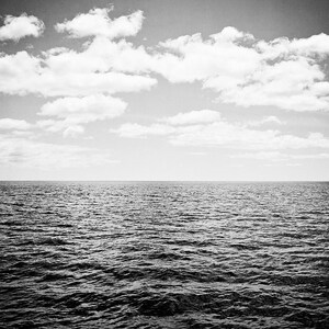Puede incluir: Fotograf&iacute;a en blanco y negro del oc&eacute;ano bajo un cielo nublado. El agua oscura est&aacute; ondulada, con una l&iacute;nea de horizonte clara. El cielo est&aacute; lleno de nubes blancas y esponjosas, creando una escena natural.