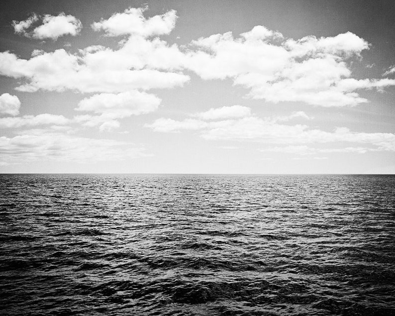 Puede incluir: Fotograf&iacute;a en blanco y negro del oc&eacute;ano bajo un cielo nublado. El agua oscura est&aacute; ondulada, con una l&iacute;nea de horizonte clara. El cielo est&aacute; lleno de nubes blancas y esponjosas, creando una escena natural.