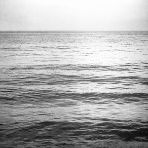 Puede incluir: Fotograf&iacute;a en blanco y negro del oc&eacute;ano. La imagen captura el mar con suaves olas bajo un cielo brumoso, creando una est&eacute;tica serena y minimalista. La l&iacute;nea del horizonte es claramente visible.
