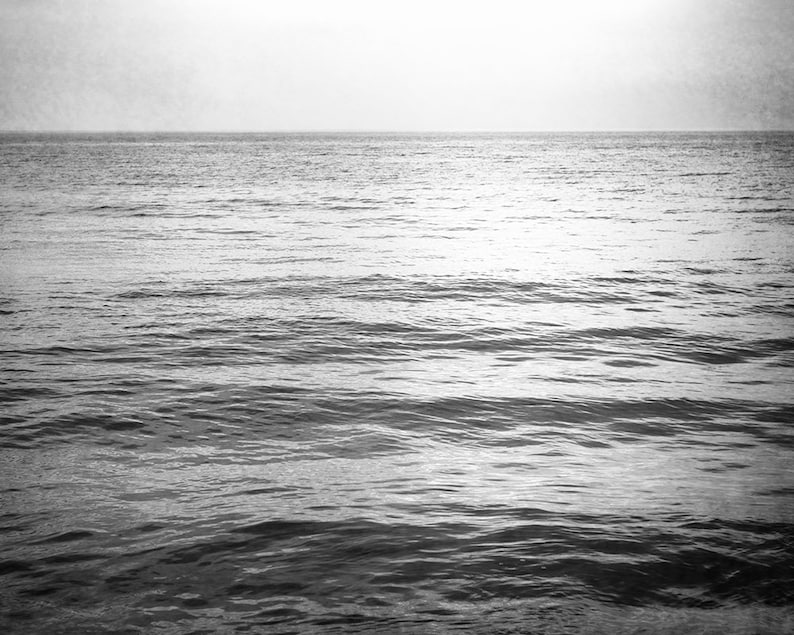Puede incluir: Fotograf&iacute;a en blanco y negro del oc&eacute;ano. La imagen captura el mar con suaves olas bajo un cielo brumoso, creando una est&eacute;tica serena y minimalista. La l&iacute;nea del horizonte es claramente visible.