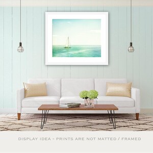 May include: A framed print of a sailboat on the ocean hangs above a white sofa with yellow pillows. A wooden coffee table with black hairpin legs sits on a patterned rug. The wall is painted a light blue.