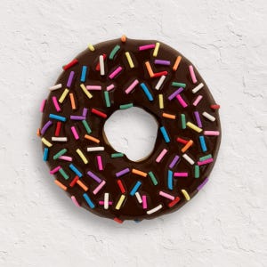 May include: A chocolate-glazed doughnut with colourful sprinkles. The doughnut is round with a hole in the middle and is covered in a glossy, dark brown glaze. The sprinkles are various colours, including red, orange, yellow, green, blue, and purple.