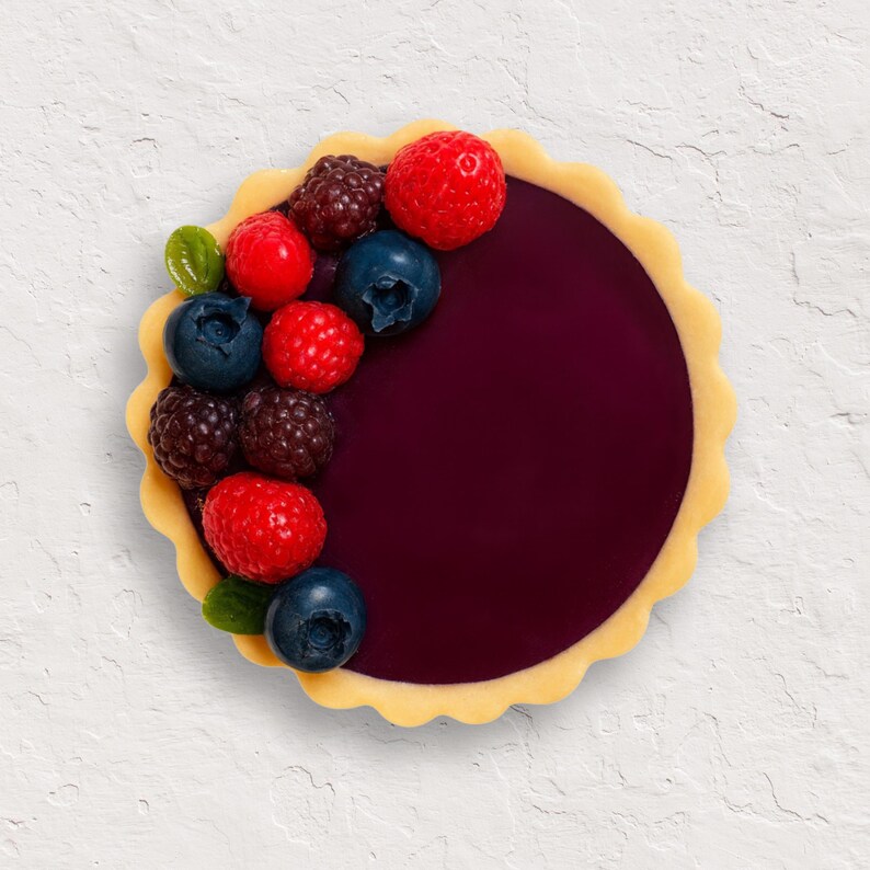 May include: A circular pastry tart with a dark purple filling and a scalloped edge. The tart is adorned with fresh blueberries, raspberries, and blackberries, with a few green leaves. The dessert is presented on a white background.