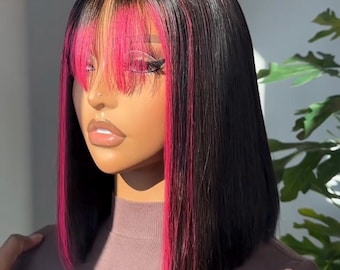 May include: A black bob wig with a vibrant pink fringe and highlights. The wig features a blunt cut and a natural-looking hairline. The hair is styled with a sleek, straight texture, and the pink accents add a pop of color.