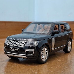 Puede incluir: Maqueta de SUV negra con detalles plateados y ruedas cromadas. La parrilla delantera es plateada y la matrícula dice "CHE ZHI". El coche de juguete está sobre una superficie de madera.