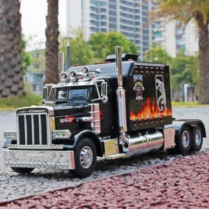 May include: A black toy semi-truck featuring a chrome front grille, bumper, and exhaust stacks. The side of the truck cab displays a flame graphic, a white animal silhouette, and text that reads Heavy Truck and Speed in red lettering.