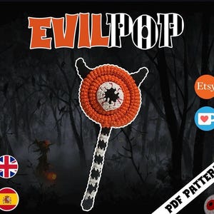 Peut inclure: Un modèle au crochet représentant un objet en forme de sucette avec un dessus en spirale orange, deux petites cornes noires et un centre blanc avec une pupille noire et des veines rouges. Le manche est rayé noir et blanc. Texte EVILPOP.